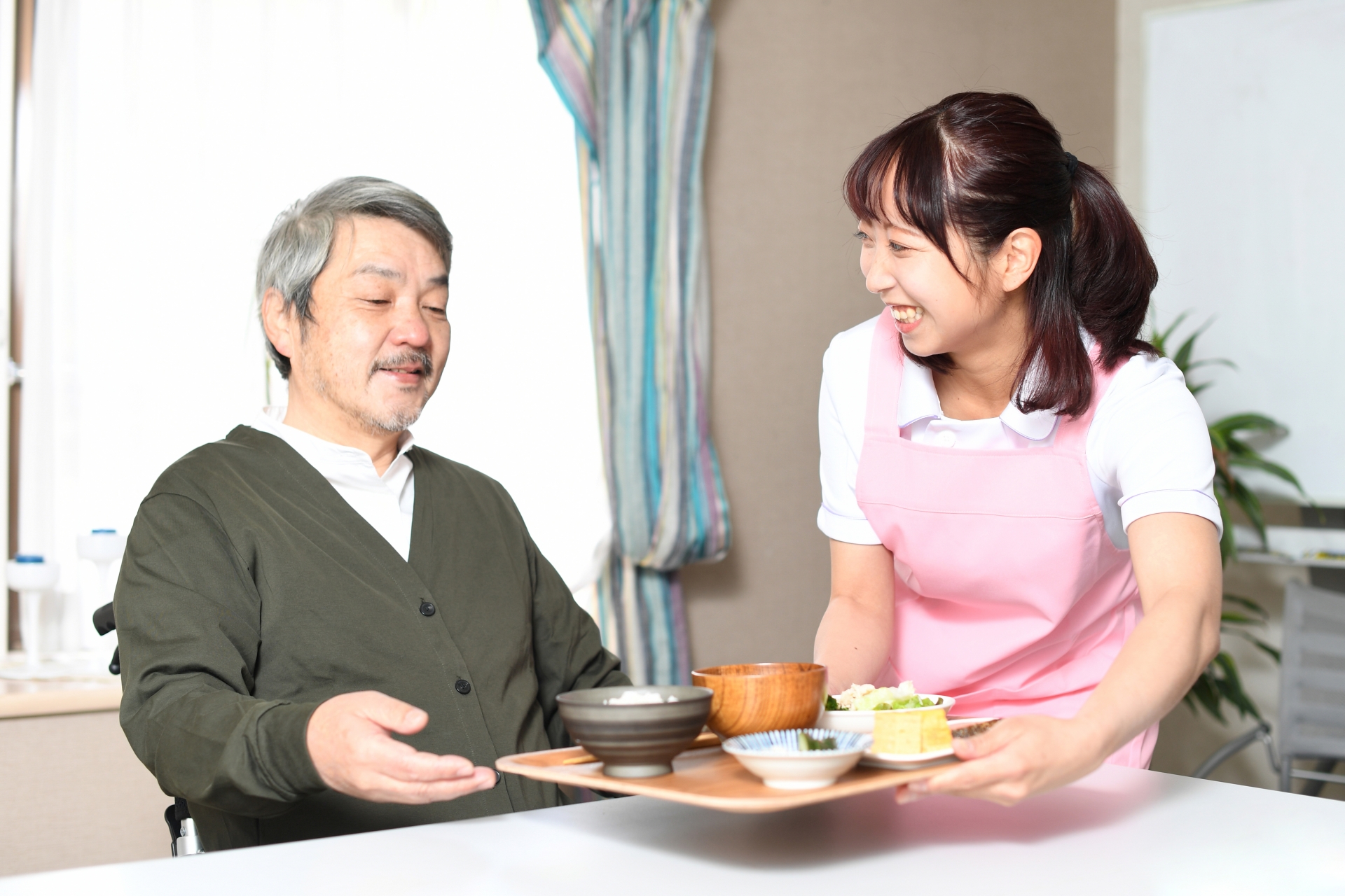 食事の配膳をする女性介護士と高齢者男性